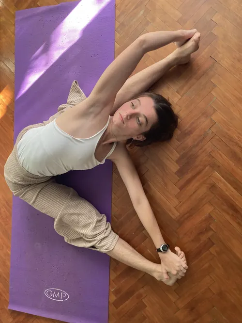 Vista desde arriba: Eugenia practica en su casa sobre un mat, con una flexión lateral tomándose los pies.