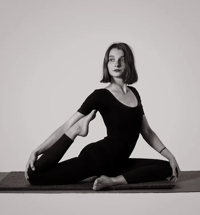 Fotografía en blanco y negro: Eugenia sentada sobre el mat en una postura de apertura de cadera, con la mirada serena.